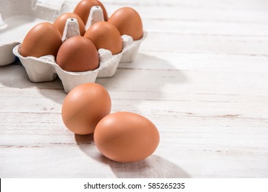 Close-up view of raw chicken eggs in egg box on white wooden background
