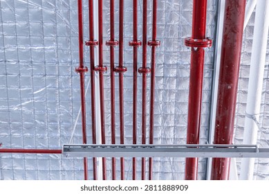 Close-up view of red fire sprinkler system pipes installed on an insulated ceiling in an industrial or commercial building.