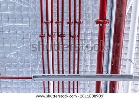 Close-up view of red fire sprinkler system pipes installed on an insulated ceiling in an industrial or commercial building.