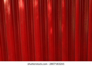 A close-up view of a red textured plastic surface featuring repeating vertical patterns and glossy reflections. The vibrant red color and geometric design create a bold abstract background suitable for graphic design, product mockups, packaging concepts, and modern decorative applications. The image emphasizes texture, symmetry, and contemporary design aesthetics