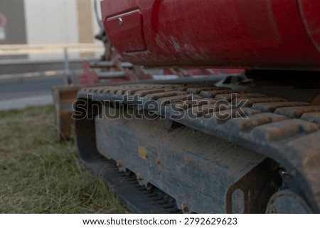 Close-up view of a red tracked construction machine showing the metal undercarriage, heavy treaded track, worn surface, and grassy outdoor setting