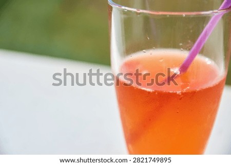Close-up view of a refreshing orange spritz cocktail in a tall glass with condensation droplets and a purple straw on a white surface.