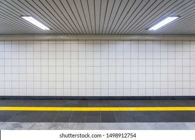 Closeup View of a Regular Public Corridor. Nobody is in the Tunnel with White Square Tiles, Yellow Tactile Paving and White Ceiling Lights.