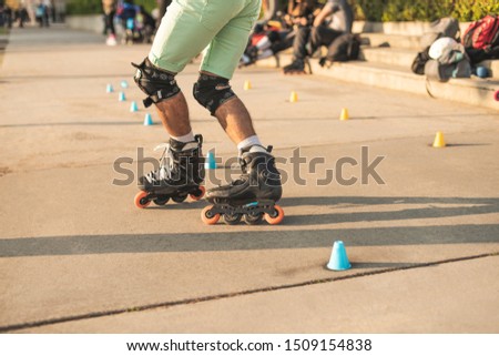 Close-up view of the rollers of a caucasian man, doing rollerblading, inline skating, performing on a slalom course on asphalt surface. Small cones for training on the road.