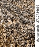 ​A close-up view of a rough, coarse-grained igneous rock, likely granite, showing its crystalline structure and varied colors.