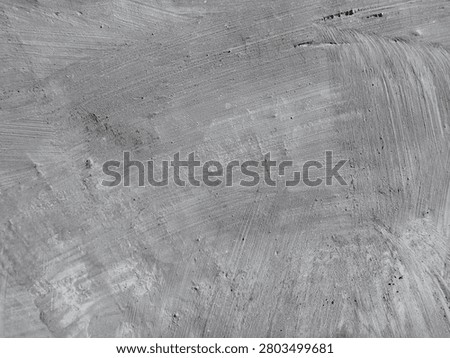 ​A close-up view of a rough, textured grey concrete wall showing visible brush strokes and surface imperfections.