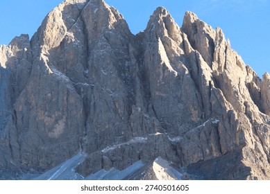 A close-up view of the rugged and dramatic peaks of the Dolomites, showcasing the sharp, jagged cliffs with snow-capped ridges against a clear blue sky.