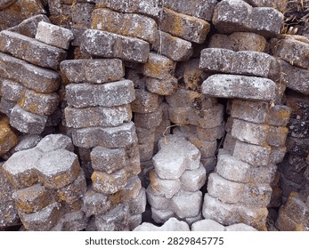 A close-up view of a rugged stack of concrete and sand paving blocks, showcasing a blend of construction history. This pile features a mix of freshly molded, pale grey blocks alongside older, weathered ones that have clearly seen previous service on a walkway or patio before being carefully removed and stacked for future projects