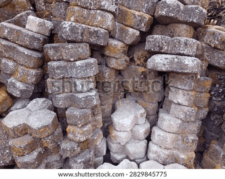A close-up view of a rugged stack of concrete and sand paving blocks, showcasing a blend of construction history. This pile features a mix of freshly molded, pale grey blocks alongside older, weathered ones that have clearly seen previous service on a walkway or patio before being carefully removed and stacked for future projects