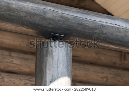 Close-up view of a rustic log cabin timber post supporting a horizontal beam, highlighting natural wood grain, joinery details and a metal plate fastener in warm, weathered architectural texture