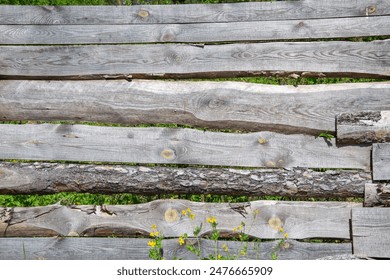 A close-up view of a rustic wooden fence with faded, gray planks and a few yellow wildflowers in the foreground. - Powered by Shutterstock