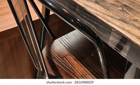 A close-up view of a rustic wooden table and chair with dark metal legs, suggesting a cozy cafe or dining setting. The textures of wood grain and polished metal are prominent.