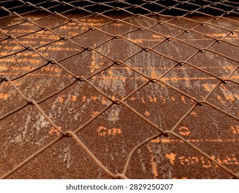 Close-up view of a rusty chain link fence over a weathered metal surface with peeling orange paint and corrosion.