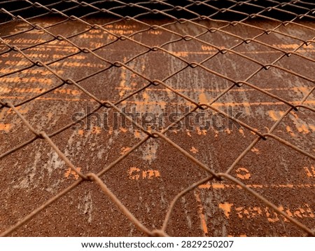 Close-up view of a rusty chain link fence over a weathered metal surface with peeling orange paint and corrosion.