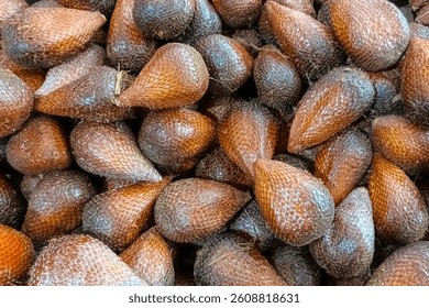 A close-up view of salak fruit, also known as snake fruit, showing its scaly brown skin and unique texture, piled together in a vibrant tropical market scene