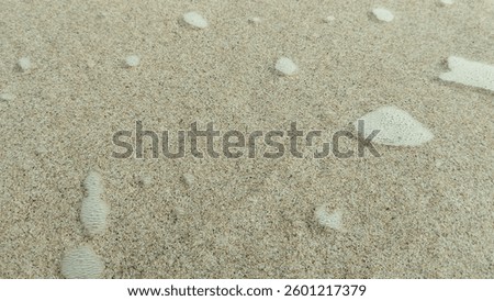 A close-up view of sandy beach texture with small watermarks left by receding waves. The natural pattern and fine grains create a serene coastal atmosphere. Perfect for backgrounds or nature-themed