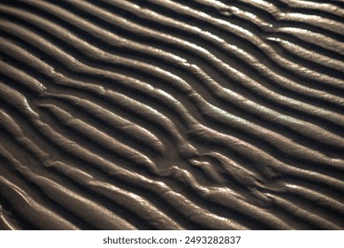 A closeup view of a sandy surface with gently moving waves in focus, creating a serene and tranquil landscape for macro photography enthusiasts