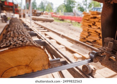 A close-up view of a sawmill with a large log being cut by a band saw. The saw blade is in focus, showing the cutting mechanism, while the log and sawmill environment are blurred in the background. - Powered by Shutterstock