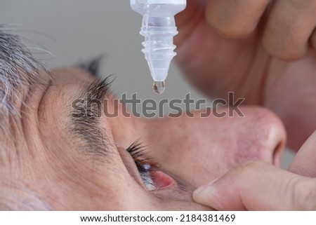Close-up view of a senior Asian adult male using eye drop in right eye after catarct surgery.