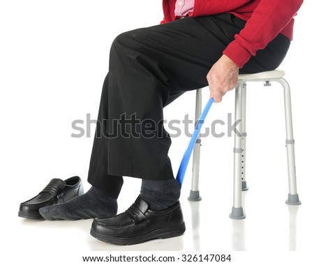 Close-up view of a senior man sliding into his loafers with the aid of a long-handled shoe horn.  On a white background.