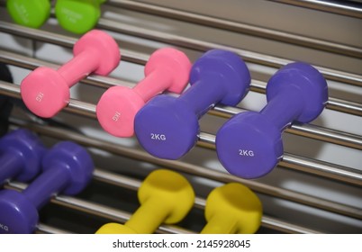 Close-up view of several purple and pink dumbbells on metal shelf in sport fitness center on a barbells background. Weight training equipment or weight loss concept.
					
					1 kg and 2 kg dumbells.