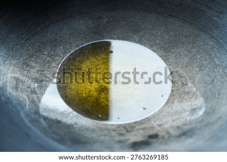 A close-up view of a shallow pan containing half oil and half water creating a distinct separation with visible surface tension and reflections under bright lighting emphasizing the contrast between