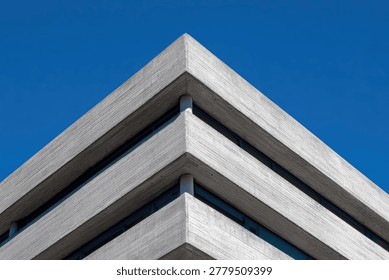 A close-up view of the sharp, geometric corner of a modern concrete building, set against a vibrant, cloudless blue sky.