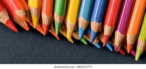 Close-up view of sharpened colored pencils in a variety of bright colors, artfully arranged on a dark, textured background, suggesting creativity and artistic expression.