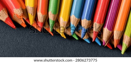 Close-up view of sharpened colored pencils in a variety of bright colors, artfully arranged on a dark, textured background, suggesting creativity and artistic expression.