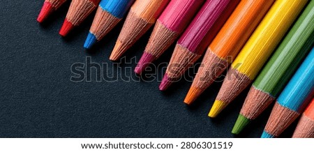 Close-up view of sharpened colored pencils in a spectrum of bright colors, laid out in a diagonal line against a dark, textured background.