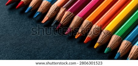Close-up view of sharpened colored pencils in a spectrum of colors, laid out in a diagonal line on a dark, textured background.