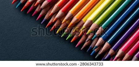 Close-up view of sharpened colored pencils in a rainbow spectrum, laid out in a diagonal pattern on a dark, textured surface.