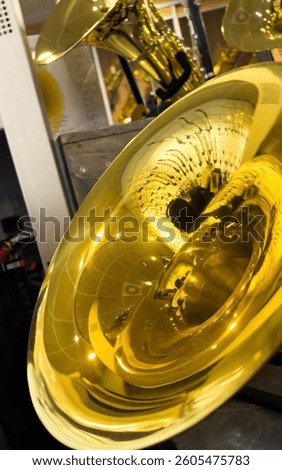 Close-up view of a shiny brass sousaphone bell reflecting ceiling tiles and lights in a well-lit music shop interior filled with various golden brass instruments on display