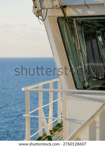 Close-up view of ship bridge structure with window and railing overlooking calm open sea. Maritime navigation and transportation concept with copy space.