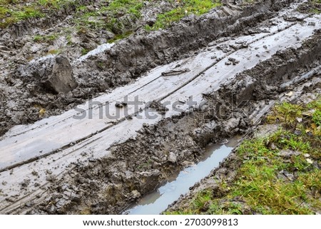 A close-up view showcasing deep ruts filled with water in a muddy country road, creating a textured and wet appearance. The image conveys challenging off-road conditions and rough, impassable terrain.