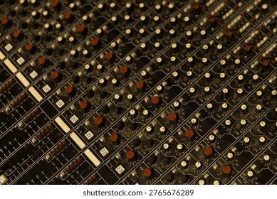 A close-up view shows a control panel used for sound mixing. Knobs and sliders are arranged in rows. The setting is a recording studio focused on music production.