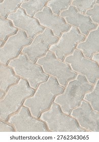 A close-up view shows an interlocking pavement made of uniquely shaped concrete bricks fitted together in a repeating pattern. The blocks have a slightly curved, zigzag-like design that locks tightly with adjacent pieces, forming a continuous, stable surface.