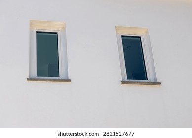 A close-up view shows two rectangular windows with dark glass set into a rough white stucco facade