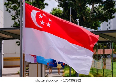 Closeup View Of Singapore Flag Waving In The Wind On Bright Sunny Day. HDB Neighbourhood In Background. Selective Focus