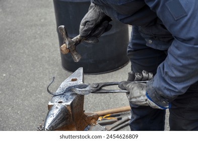 Close-up view of a skilled blacksmith with hammer and tongs ready to strike a piece of hot metal resting on an anvil - Powered by Shutterstock