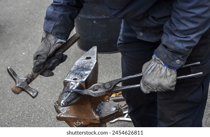 Close-up view of a skilled blacksmith with hammer and tongs ready to strike a piece of hot metal resting on an anvil - Powered by Shutterstock