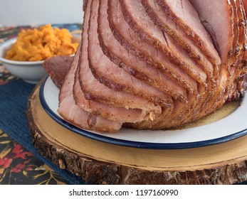 A Closeup View Of The Slices Falling Away From A Glazed And Freshly Baked Spiral Cut Ham, With A Bowl Of Mashed Yams In The Background