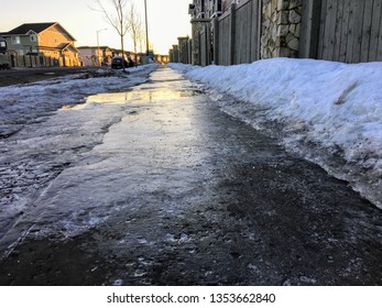 A Closeup View Of Slippery Black Ice Covering A Sidewalk In The Early Morning Of A Residential Neighbourhood During The Winter In Edmonton, Alberta, Canada.