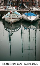 Close-up view of small Italian white boats moored to a wooden pier with the reflection of long masts on the surface of Lake Garda in Desenzano del Garda, Province of Brescia, Italy.