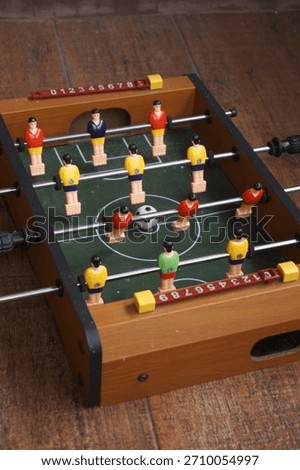 A close-up view of a small tabletop foosball game featuring colorful plastic players, metal rods, and a soccer ball on a miniature field. The playful setup captures themes of recreation, leisure, team