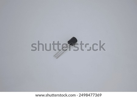A close-up view of a small transistor with three metal leads, isolated against a plain background. This essential electronic component is used to amplify and switch electronic signals.