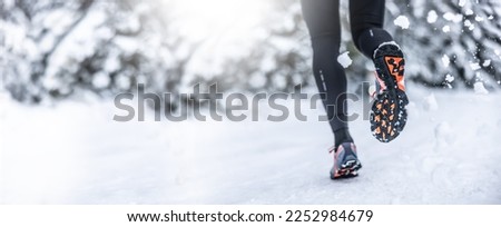 A close-up view of the sneakers of a running woman during training on the snow in the winter season. Banner with copy space.