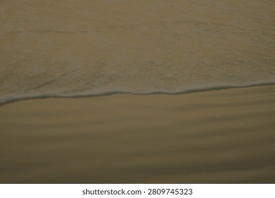 Close-up view of a soft wave cresting and receding on a wet sandy shore, bathed in the warm hues of twilight