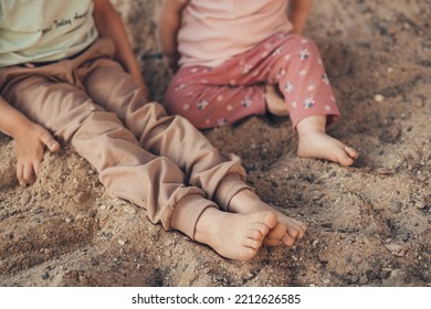 Close-up View Of Some Children's Feet Sitting Barefoot On The Cold Sand In The Village Garden. Cute Children Playing In Sand On Outdoor Playground. Sunny Warm