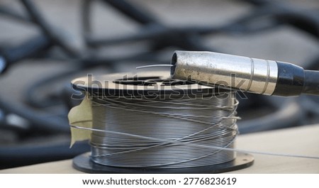 Close-up view of a spool of welding wire with a MIG gun nozzle positioned above it, suggesting preparation for industrial repair or construction